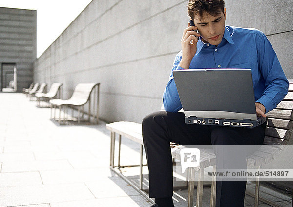 Man sitting on bench with cell phone and laptop