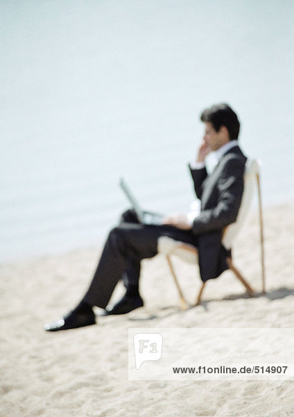 Geschäftsmann am Strand sitzend mit Laptop auf Knien,  durchgehend,  Nahaufnahme,  verschwommen