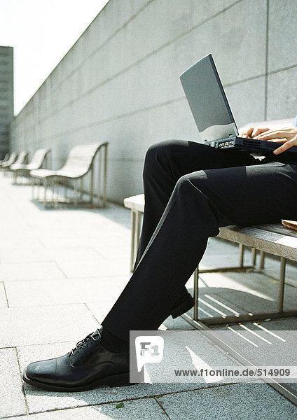 Mann auf Bank mit Laptop auf Knien  Nahaufnahme