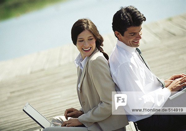 Geschäftsmann und Frau Rücken an Rücken mit Laptop-Computern,  Taille nach oben,  Neigung