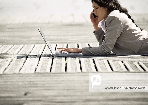 Geschäftsfrau auf dem Bauch liegend mit Laptop  im Freien