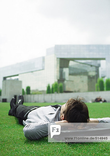 Geschäftsmann auf Gras liegend mit Kopf auf Aktentasche