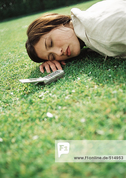Frau auf Gras liegend mit Handy am Kopf  Nahaufnahme