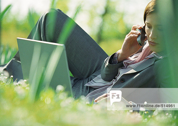 Geschäftsfrau auf Rasen liegend mit Laptop und Handy