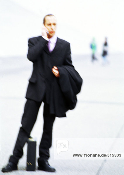 Businessman with briefcase in hand  using cell phone