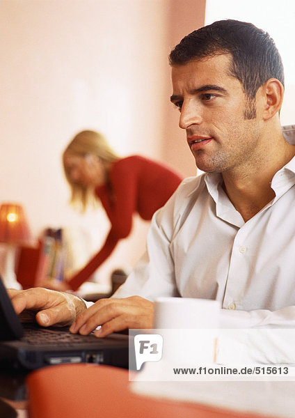 Mann arbeitet am Computer  Frau im Hintergrund am Telefon.