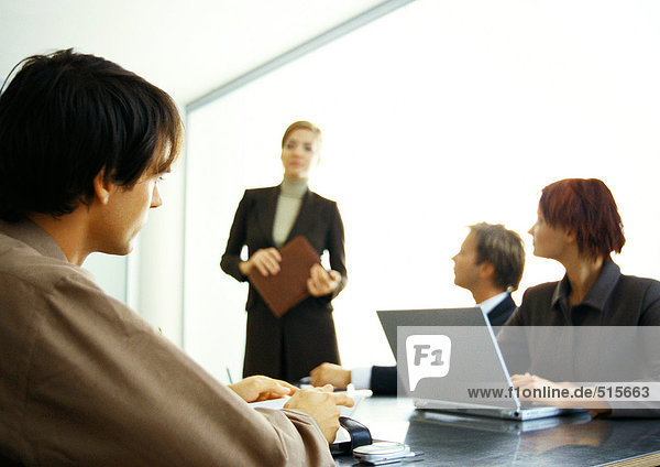 Business people around table looking at businesswoman standing