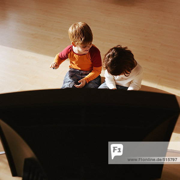 Kinder sitzen gemeinsam auf dem Boden  Fernsehen im Vordergrund
