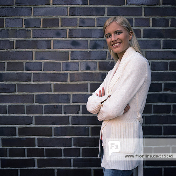 Woman smiling at camera  standing next to brick wall  portrait