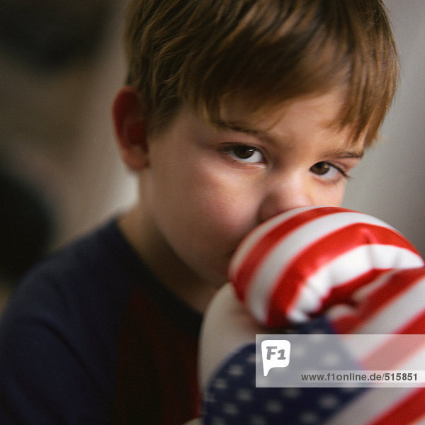 Kleiner Junge  der den Mund mit Boxhandschuhen bedeckt  Portrait