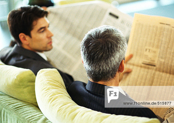 Businessmen sitting reading newspapers  rear view  head and shoulders