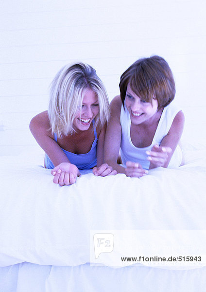 Two women lying on stomachs on bed  laughing