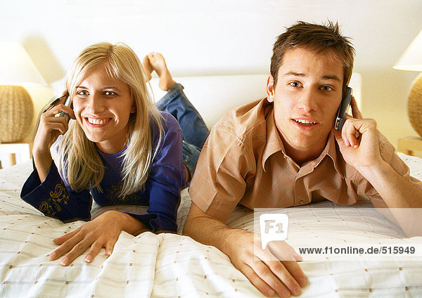 Couple reclining on bed  both using cell phones