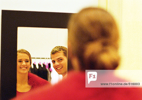 Woman trying on coat  smiling at boyfriend in mirror