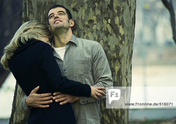 Couple leaning against tree trunk  embracing