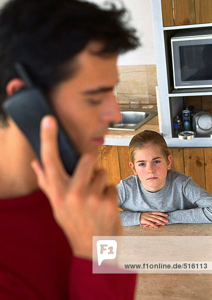 Kind schaut Vater am Telefon in der Küche an  verschwommen.