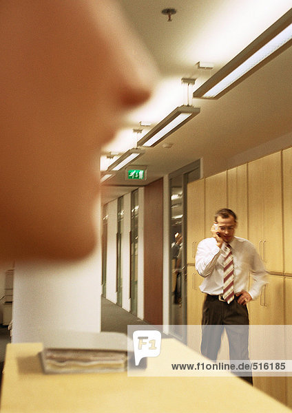 Businessman on phone walking down hallway  person's face blurred in foreground