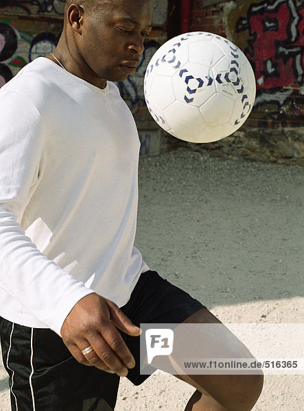 Mann jongliert mit Fußball vor graffitierter Wand