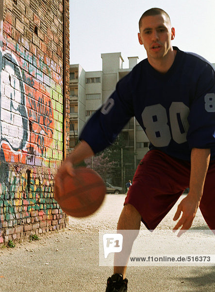 Mann dribbelt Basketball im städtischen Spielplatz neben der Graffiti-Wand