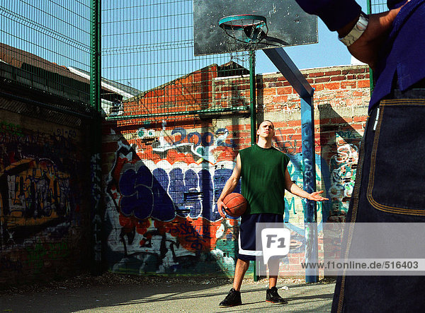 Mann hält Basketball  Arm aus  schaut auf den zweiten Mann.