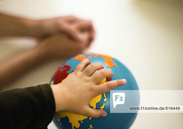 Kinderhand auf Globus  gefaltete Hände im Hintergrund