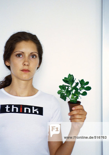 Porträt einer Frau  die eine kleine Topfpflanze mit der Hand hochhält.