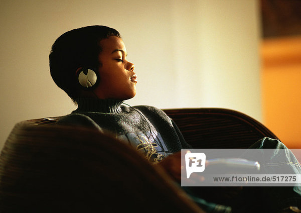 Junge sitzt im Stuhl und hört Musik mit geschlossenen Augen und Kopfhörern.