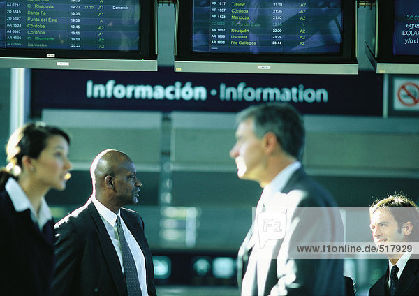 Geschäftsleute im Gespräch vor einem Flughafen-Informationsschild.