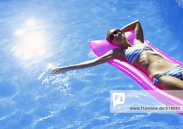Frau beim Sonnenbaden auf Luftmatratze im Pool