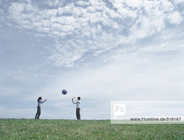 Junger Mann und Frau  die in der Ferne auf Gras stehen und den Ball werfen.