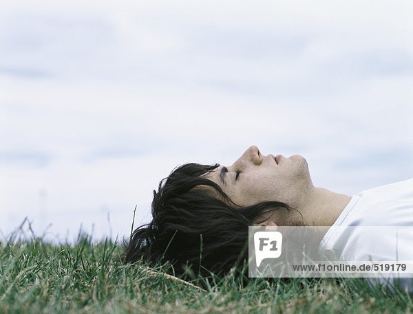Junger Mann auf dem Rücken im Gras liegend mit geschlossenen Augen  Kopf und Schultern
