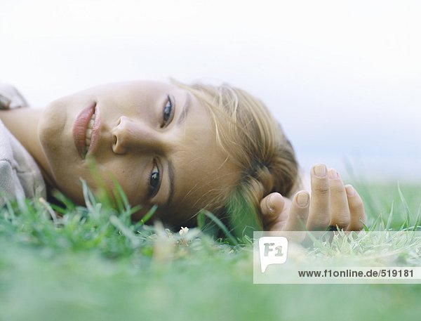 Junge Frau auf dem Rücken auf Gras liegend mit Hand über Kopf  Kopfschuss