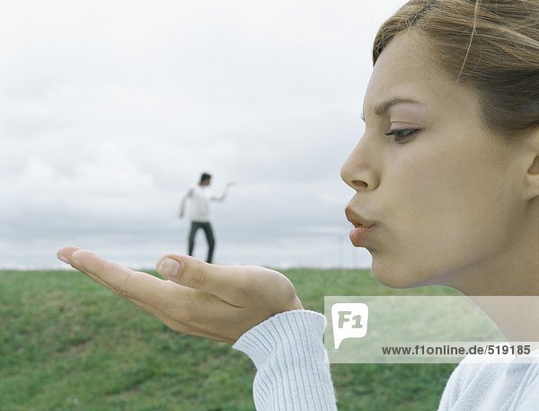 Frau im Vordergrund mit ausgestreckter Handfläche und blasendem Kuss  Mann im fernen Hintergrund  optische Täuschung