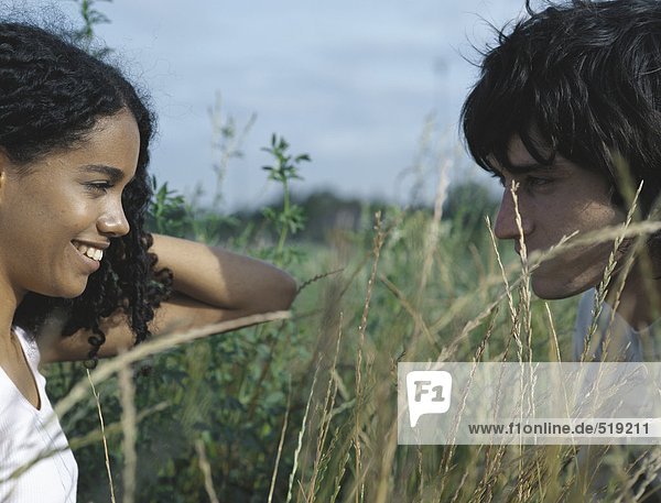 Junge Frau und junger Mann von Angesicht zu Angesicht im hohen Gras