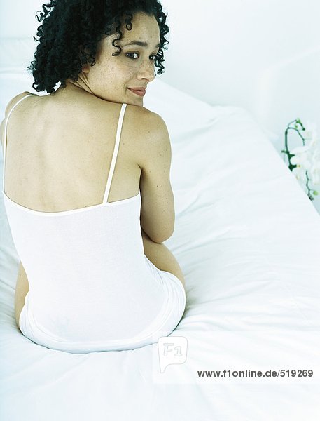 Frau sitzt auf dem Bett  trägt Unterwäsche  schaut über die Schulter  Rückansicht