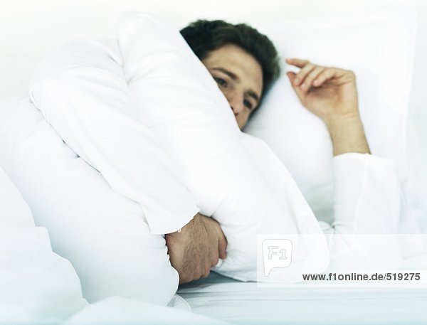 Man lying in bed on side holding pillow