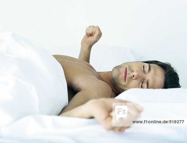 Man lying shirtless on bed  stretching arms to the side  eyes closed