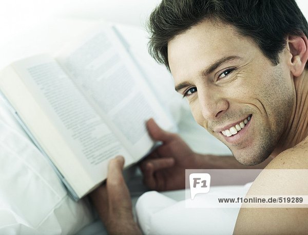 Man lying on stomach holding book  looking over shoulder at camera  close-up