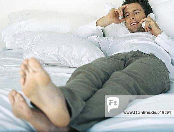 Clothed man lying on bed talking on cordless phone  hand to head