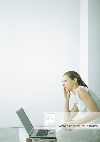 Junge Frau auf dem Boden sitzend mit Laptop  hält Handy an Ohr