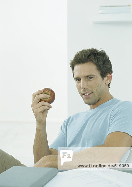 Junger Mann sitzt am Tisch und hält den Apfel in der Hand.