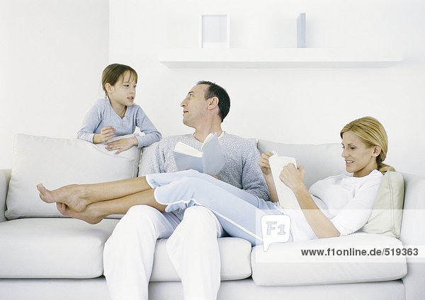 Parents sitting on sofa  girl standing behind sofa talking to father