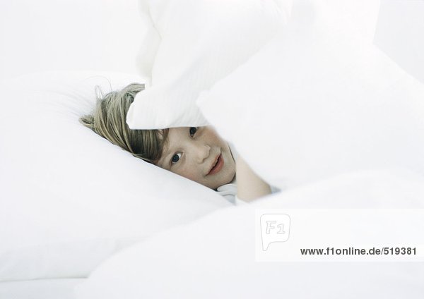 Little boy in bed  looking through pillows