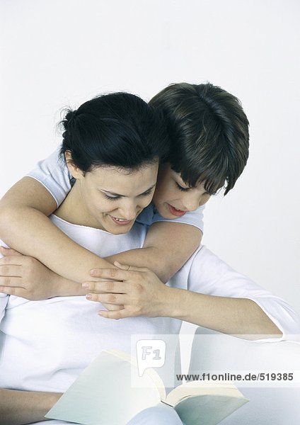 Woman and son reading book  boy with arms around woman  looking over her shoulder
