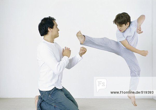 Boy giving karate kick in mid air  man on knees with fists out