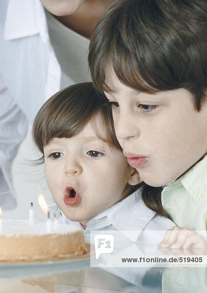 Junge und kleines Mädchen blasen Kerzen auf Kuchen aus  Mutter im Hintergrund
