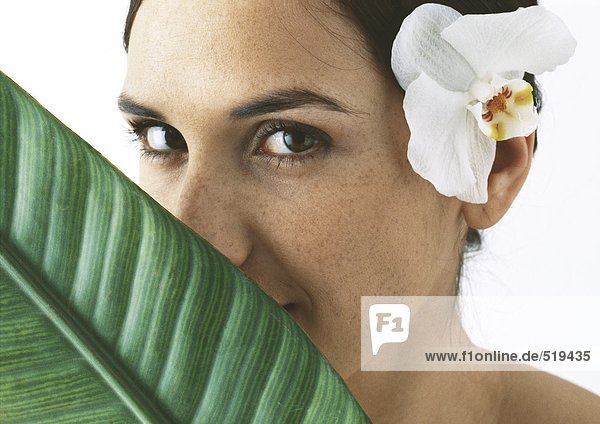 Frau mit Orchidee hinter dem Ohr  Palmblatt teilweise das Gesicht bedeckend  Nahaufnahme