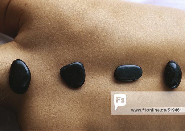 Frauenrücken mit schwarzen Steinen entlang der Wirbelsäule  Nahaufnahme
