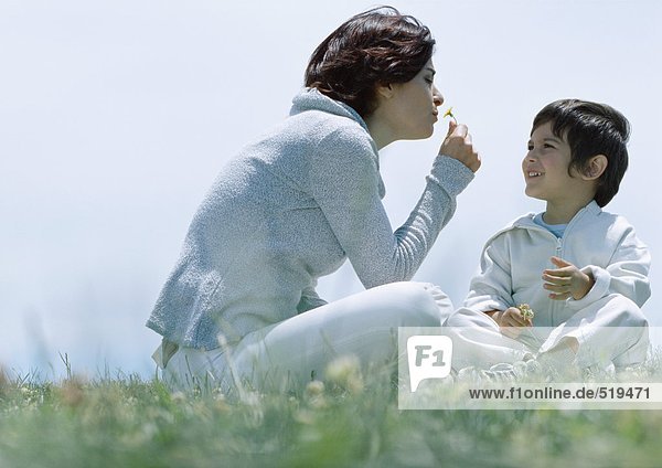 Frau und Sohn sitzen auf Gras  Frau riecht Blume