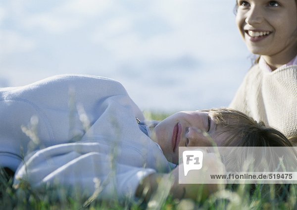 Junge auf Gras liegend mit geschlossenen Augen  Mädchen hinter ihm